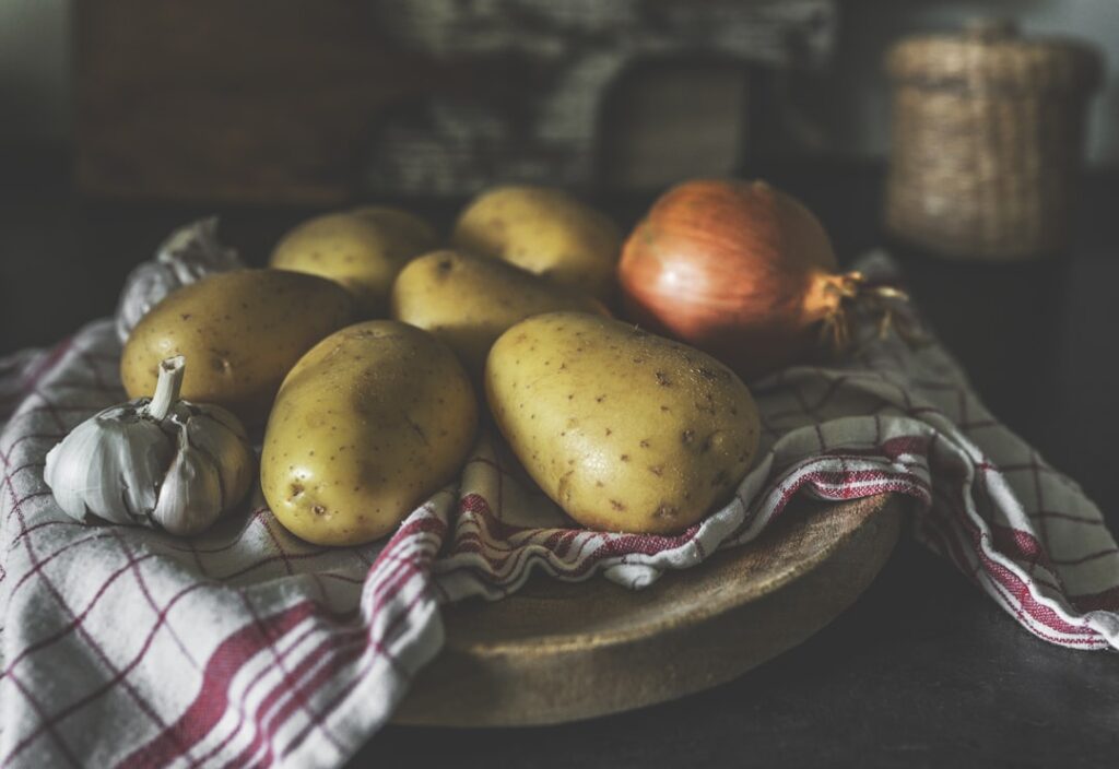Raw potatoes, onion, and garlic arranged on a wooden board with a striped cloth — all prebiotic foods whose fiber changes with cooking