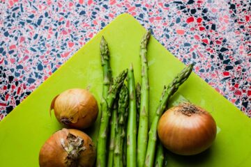 Flat-lay of asparagus spears and whole onion bulbs on a green cutting board — key prebiotic foods rich in inulin and FOS