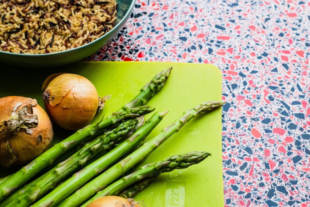 Asparagus spears and onion bulbs on a cutting board beside a bowl of grains — classic prebiotic inulin and FOS sources