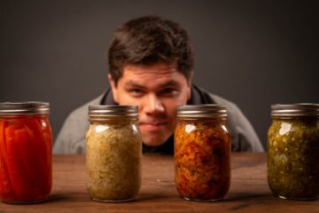 Person inspecting jars of fermented vegetables including sauerkraut on a wooden table