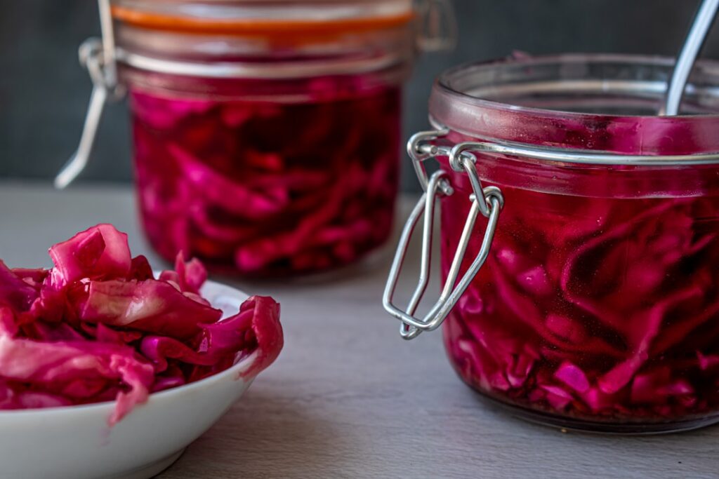 Clamp-lid glass jars filled with red fermented cabbage sauerkraut alongside a small bowl of the same