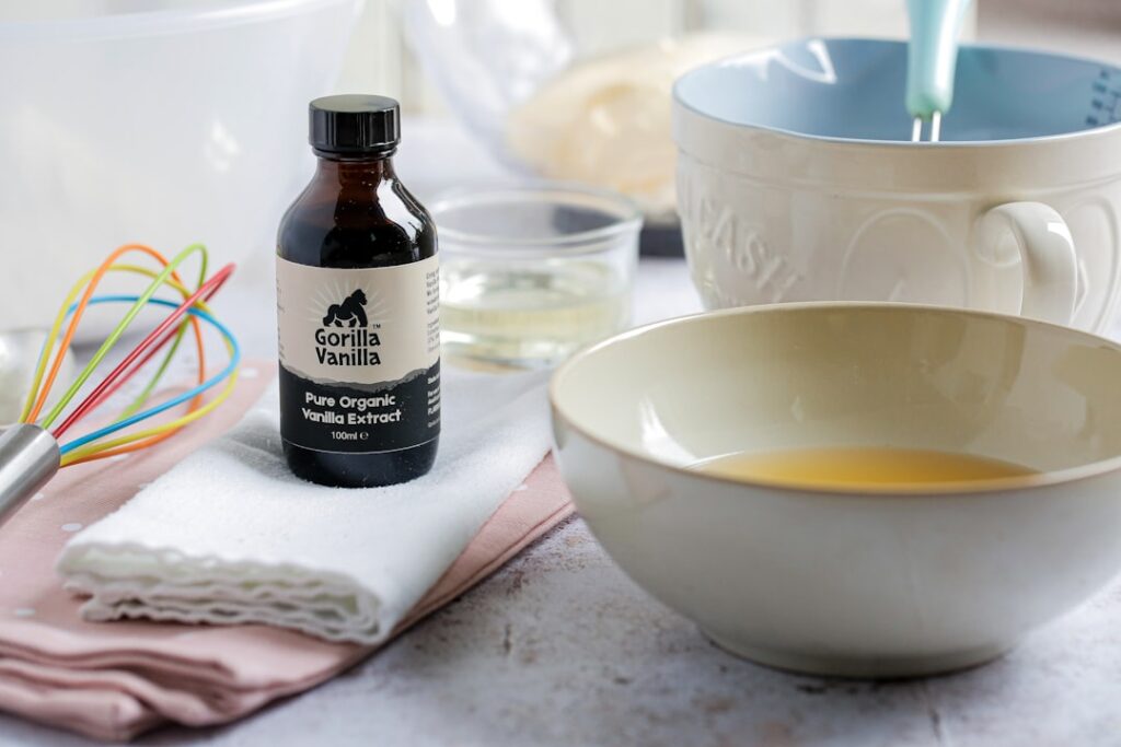 A bottle of pure organic vanilla extract beside baking bowls and a whisk, contrasting real vanilla extract with cheaper imitation alternatives