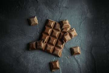 Broken chocolate bar pieces scattered on a dark stone surface — flat-lay food photography