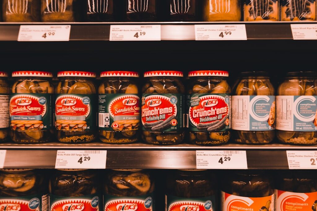 Jars of pickled cucumbers and fermented-style products sitting on a grocery store shelf at room temperature — a sign they are likely pasteurized