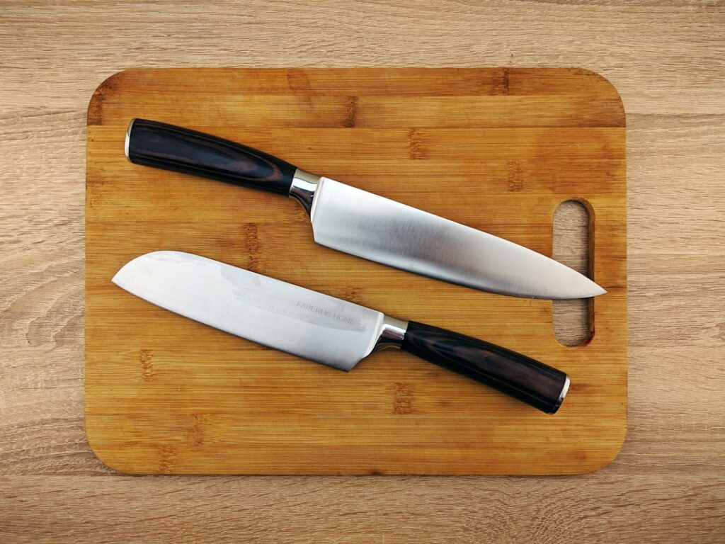 Two sharp chef's knives laid on a bamboo cutting board — a sharp blade ruptures far fewer onion cells than a dull one, reducing tear-inducing vapor