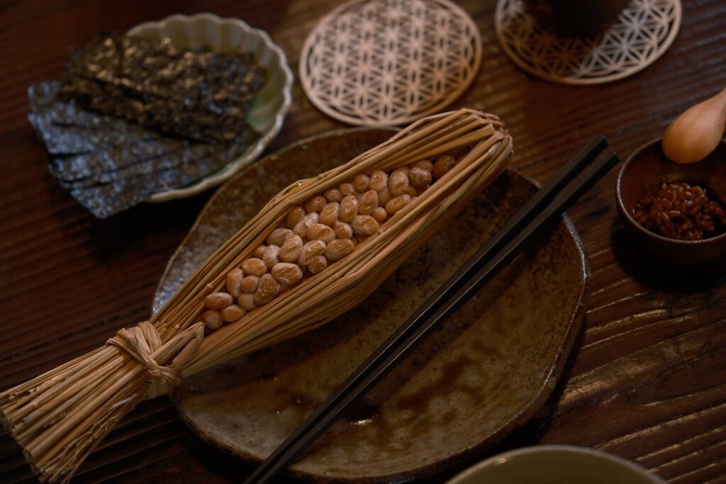 Natto fermented soybeans in traditional rice straw wrapping, served on a Japanese ceramic plate with chopsticks and condiments