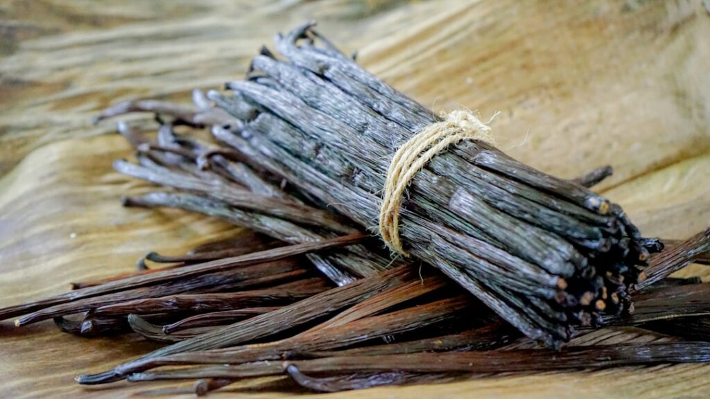 A bundle of dark cured vanilla beans tied with twine resting on a wooden surface, representing the finished product after months of drying and conditioning