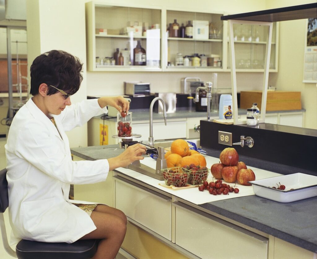 A food laboratory technician in a white coat working with food samples and equipment, circa 1970