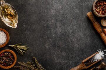 Spices, salt, herbs, and rolling pin on a dark stone kitchen surface — illustrating food science ingredients