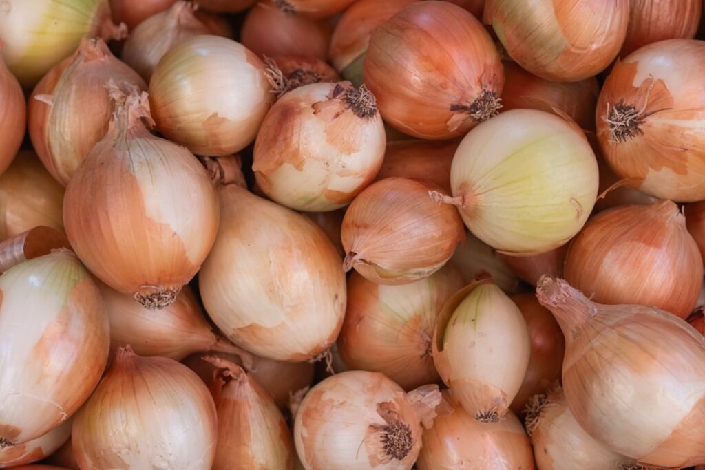 A large pile of pale golden sweet onions at a market, showing the variety associated with lower sulfur content and fewer tears when cut