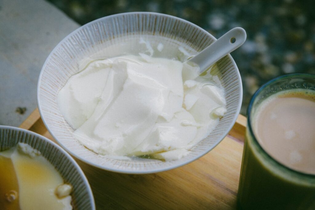 A bowl of thick white yogurt with a spoon alongside a cup of kefir drink, illustrating the texture difference between the two fermented dairy products