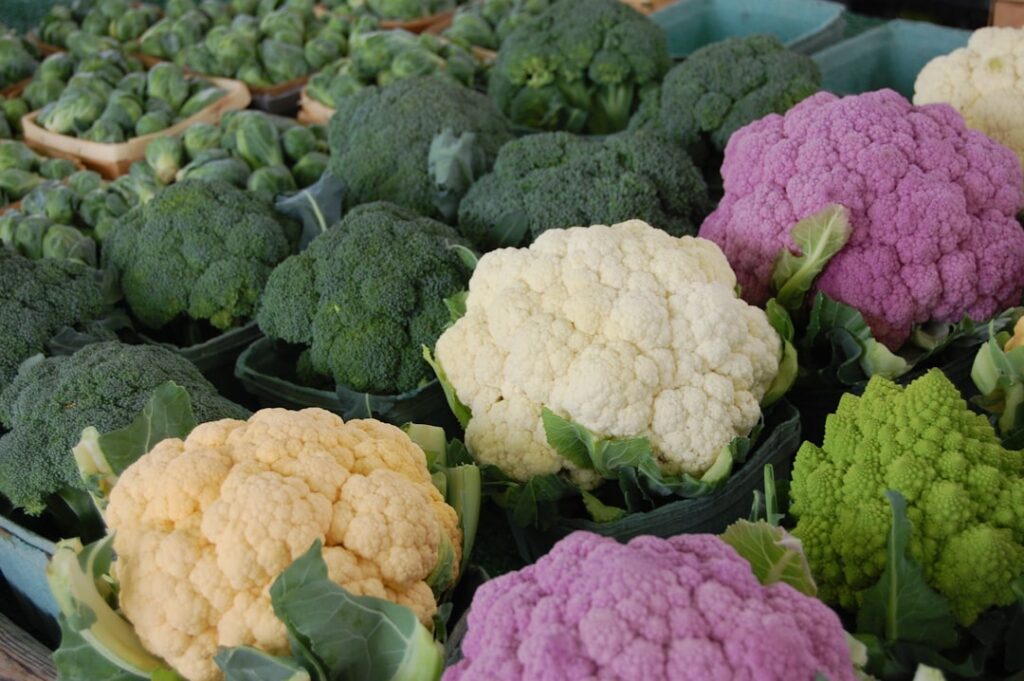 Colorful varieties of cauliflower and broccoli displayed fresh at a farmers market stall