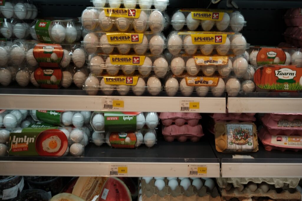 Supermarket shelves stacked with white and brown egg cartons displaying price tags, showing the price difference between egg varieties
